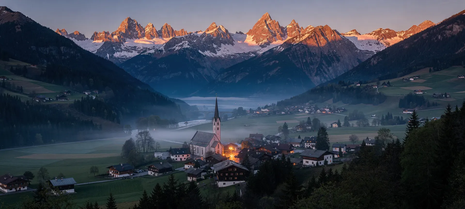Tyrolean valley at dusk with a village, church tower and glowing mountain peaks